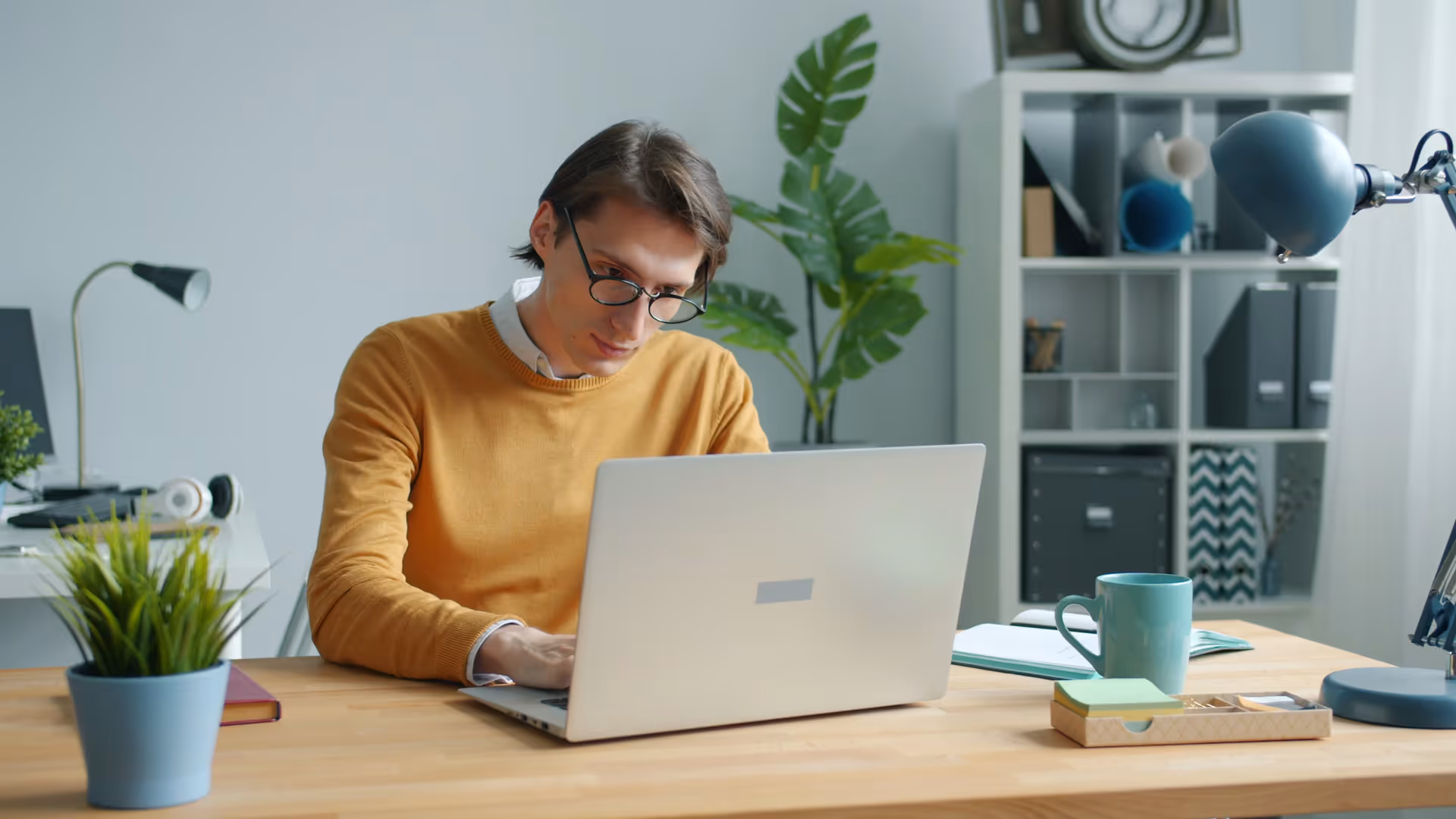 Business owner with glasses in yellow sweater working at laptop reviewing Facebook Ads budget